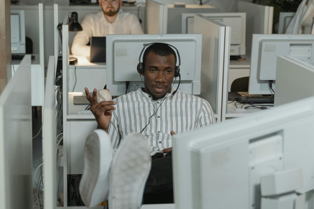 Man relaxing in office cubicle wearing headphones, holding a stress ball.