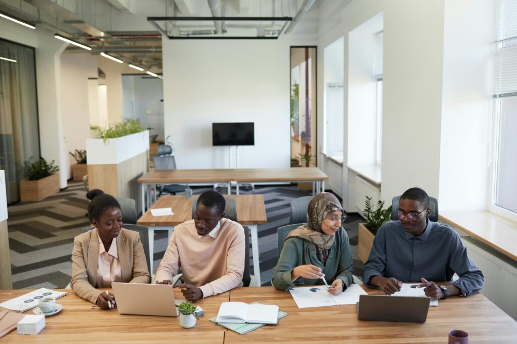 A diverse group of colleagues collaborating in a modern office setting at a wooden desk.